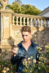 portrait of handsome brunette man wearing fantasy medieval prince costume, romantic silk shirt & royal  golden crown, posing in  castle location  rose garden with dreamy golden  silhouette lighting