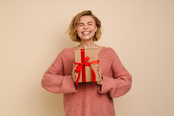 Woman holding gift box and screaming with joy isolated over beige wall