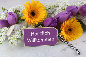 Blumenarrangement mit dem Text Herzlich Willkommen.