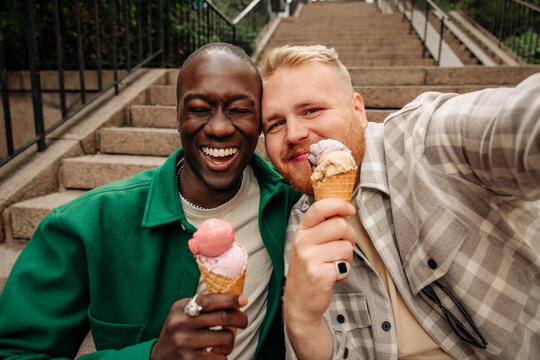 Happy male friends taking selfie while holding ice creams on steps