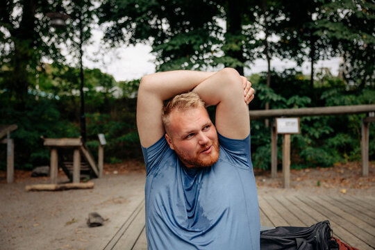 Obese man looking away while doing stretching at park
