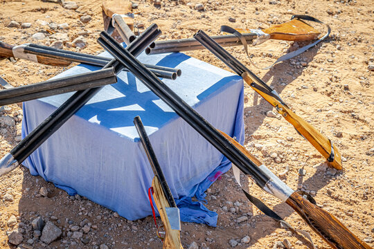 Old traditional black powder rifles exposed outdoors on the sandstone soil ground in an Algerian sahara desert market. A blue cloth covers a cube and acts as a support.