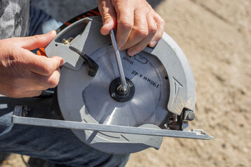 a man screws a saw blade with a hexagon on a circular miter saw