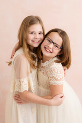Sister's hugging indoors against pink backdrop