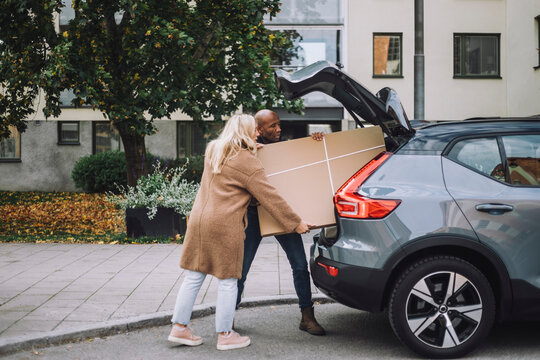 Man and woman loading cardboard together in car trunk