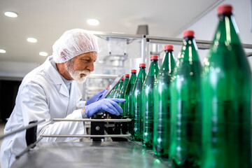 Experienced bottling plant worker controlling process of water production on conveyor machine.