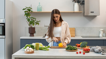  A woman cuts a pepper for a vegetable salad, standing in the kitchen. Vegetarianism
