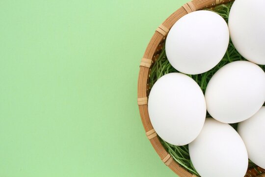 Fresh chicken eggs in wooden rattan wicker basket on green background. Natural healthy nutrition organic farm food product concept. World egg day, easter holiday composition. Close-up, flatlay