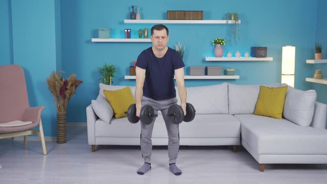 Weak, inexperienced man working out with equipment at home.
Inexperienced powerless man trying to make body at home with the help of equipment.
