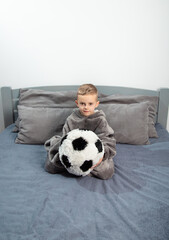 A six-year-old boy plays with a stuffed toy in the form of a soccer ball on the bed.A six-year-old boy plays with a stuffed toy in the form of a soccer ball on the bed.hugs the ball