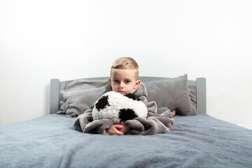 A six-year-old boy plays with a stuffed toy in the form of a soccer ball on the bed.A six-year-old boy plays with a stuffed toy in the form of a soccer ball on the bed.hugs the ball