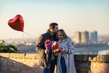 Happy couple with a gift, flowers and a balloon. The woman is surprised and overjoyed because of...