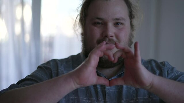 One young chubby man doing heart symbol with hands indoors. Happy person signaling love and empathy concept