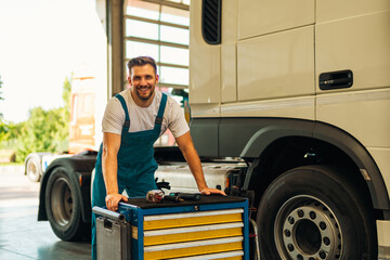 Portrait of positive smiling truck serviceman with tools standing by truck vehicle in workshop. Truck vehicle maintenance and servicing.
