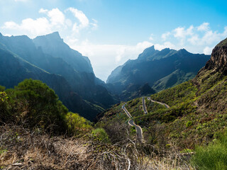 Picturesque landscape with winding curvy mountain road towards Masca village. Green valley, ocean, massive cliffs and sharp rock formation. Tenerife, Canary Islands, Spain. sunny winter day, blue sky