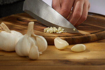 Obraz na płótnie Canvas garlic on a wooden chopping board close-up. a knife grinds a clove of garlic surrounded by whole ones. kitchen on a sunny day. High quality photo