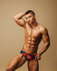 Handsome guy in swimwear posing in studio. Sexy man with six pack abs standing on neutral...