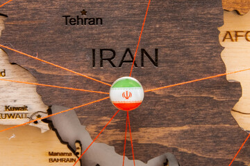 Iran flag on the pushpin and red threads on the wooden map. Travel or logistic routes. Influence in geopolitics and world economy. 