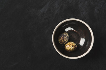 Quail eggs in ceramic bowl on black background