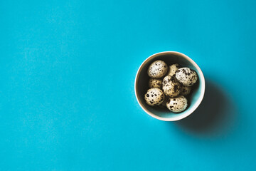 Quail eggs in a bowl on blue background
