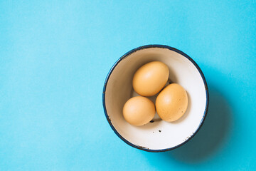 Brown chicken eggs in a bowl on blue background