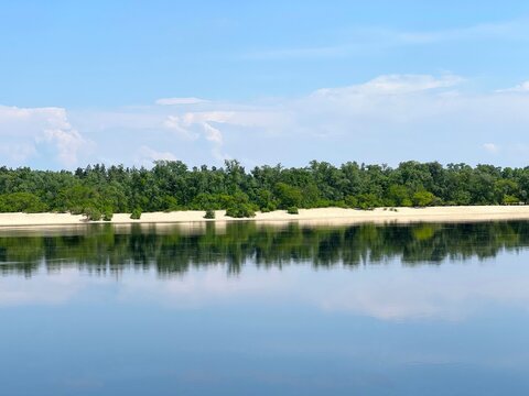 Summer river and sandy beach with trees reflections in calm blue water scenic landscape