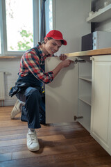 Cheerful serviceman repairing kitchen furniture in a client apartment