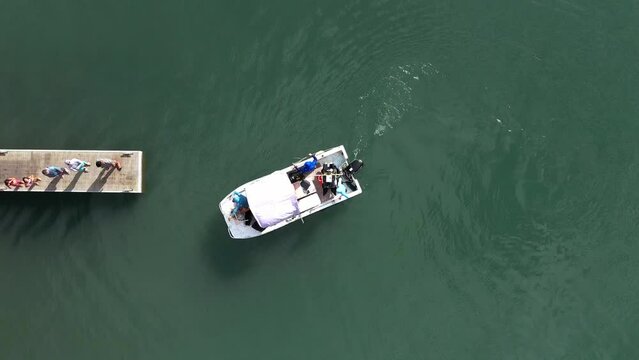 Small motorboat docking at narrow dock with people aerial straight down