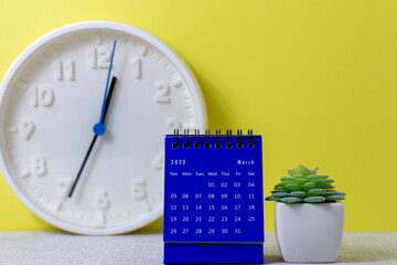 A desktop calendar for March 2023 and a clock on the table for planning your time.