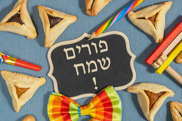 Jewish holiday Purim greeting card with traditional cookies Hamantaschen, wooden noisemaker on blue...