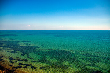 Turquoise transparent sea with algae at the bottom, taken from a cliff with ships on the horizon...