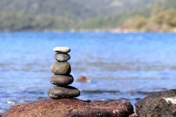 Fototapeta na wymiar Tower of pebble stones on a beach on background of green mountains. Zen balance, tranquility and travel concept