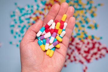 Multiple colors pills in hand on blue background. Taking Your Medication. Medicine concept.