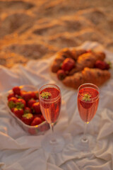 glasses of rosé wine with strawberries and croissants for two lovers. picnic on beach. still life vertical photo with free space for text