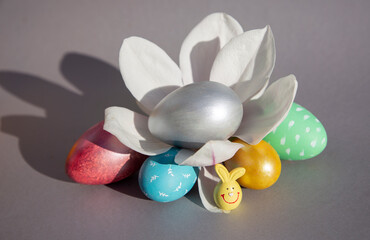 Composition with multicolored Easter eggs and a blooming large magnolia flower on a gray background illuminated by bright sunlight