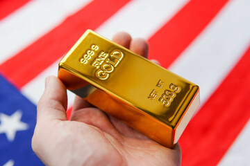The gold bar in man's hand on the national flag of USA background. Gold Reserve concept.