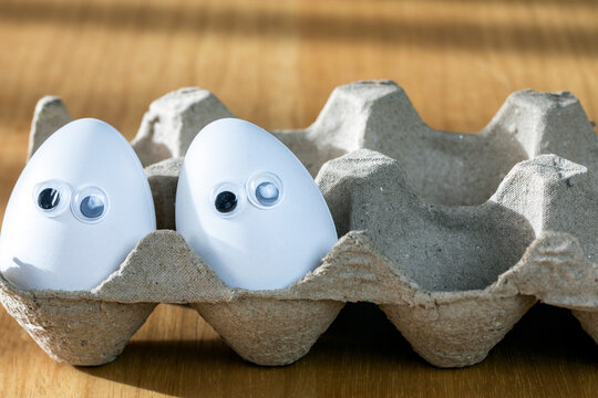 Funny faces on white eggs in carton box with organic chicken eggs on kitchen table closeup big animation eyes. humor, food and easter holiday concept.