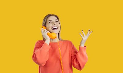 Happy young excited woman talking on landline phone isolated on yellow background. Emotional joyful caucasian woman talking on phone using wired handset orange landline retro telephone. Banner.