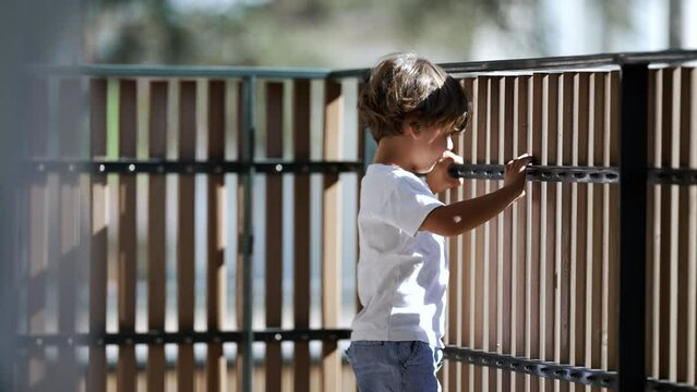 Child standing by balcony fence looking outdoors from second floor. Child holding in wooden bars staring outside