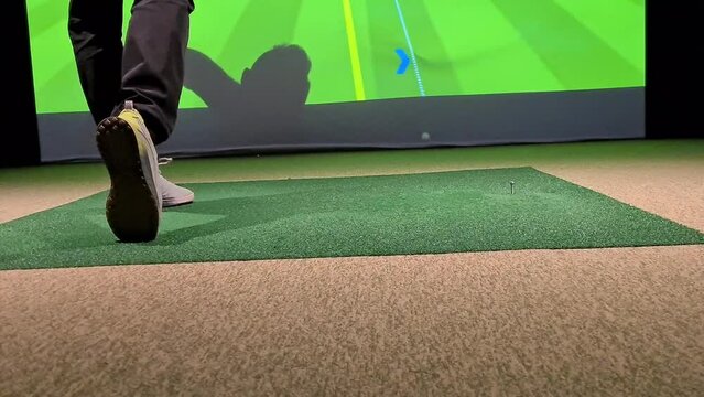 Male golfer plays golf indoors on golf simulator closeup. Driving range with screen