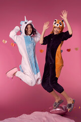 Valentine's day concept. Studio portrait of two lesbian girls in kigurumi having fun and jumping on a pink background. Cheerful girls at a pajama party.