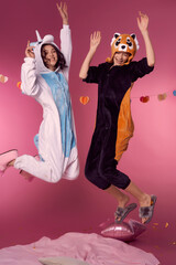 Valentine's day concept. Studio portrait of two lesbian girls in kigurumi having fun and jumping on a pink background. Cheerful girls at a pajama party.