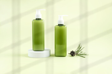 cosmetics containers on the podium, pine cone and pine branch on a light green background