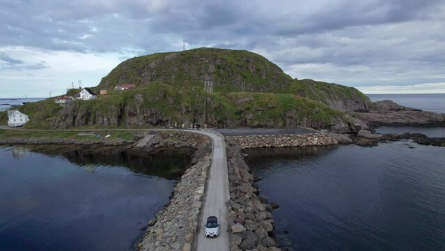Aerial drawback dolly shot of a car crossing a breakwater wall from an island on an overcast day with calm seas