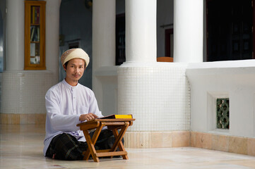 Religious muslim islam man in white session sit on the floor and read holy-Quran for praying to Allah in old mosque.concept for islamic read Quran or koran book  