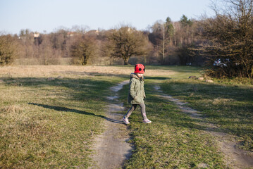 Caucasian little girl in walks in the park in the rays of the setting sun. A child in a red hat...