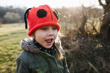 Cute baby rejoices outdoors. Portrait of a happy girl in a red hat. Children's sincere emotions.