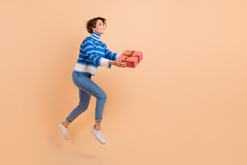 Fototapeta na wymiar Full length photo of pretty sweet lady wear blue pullover jumping giving gift empty space isolated beige color background