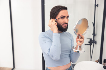 Cute young Caucasian man using eye cosmetics