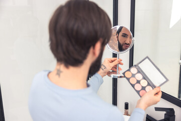 Focused guy examining his face after the blush application